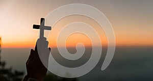 Silhouette of young woman kneeling down praying and holding christian cross for worshipping God at sunset background. concept of