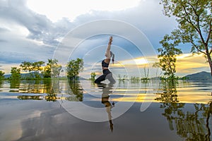 Silhouette young woman lifestyle exercising vital meditate and practicing reflect on water Flood the tree in the reservoir, backgr