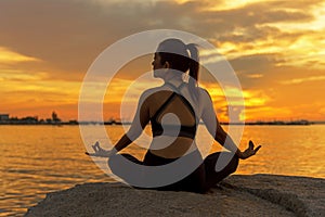 Silhouette young woman lifestyle exercising vital meditate and practicing yoga ball on the beach at sunset.