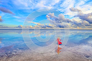 Silhouette of a young woman in a long red dress walking along the salty shore