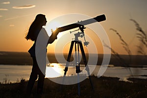 Silhouette of young woman looking view through the telescope at summer sunset