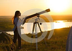 Silhouette of young woman looking view through the telescope at summer sunset