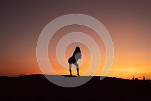 Silhouette of young woman with loose haire in front of the sunset among the desert, colorful sky on the background
