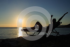 Silhouette of the young woman is lying on the deckchair at sunset