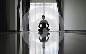 Silhouette of young woman meditating at home. Men practicing yoga indoors. Relaxation, body care, meditation, balance, fitness,