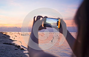 Silhouette of young woman with mobile phone camera taking picture of beautiful beach sunset landscape and mount Agung volcano of B