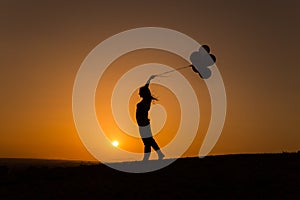 Silhouette of a young woman playing with balloons at sunset photo