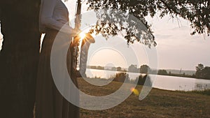 Silhouette of a young woman playing on the saxophone near the riverbank at dawn, a beautiful girl in a long dress with a wind musi