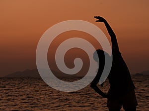 Silhouette of young woman practice yoga for healthy on sea beach at sunset in summer