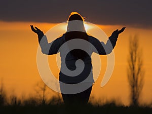 Silhouette of a young woman practicing meditation against the setting sun