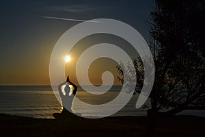Silhouette of young woman practicing yoga on the beach