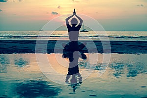 Silhouette young woman practicing yoga on the beach