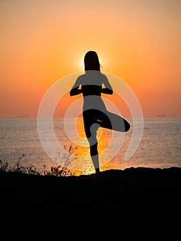 Silhouette young woman practicing yoga on the beach above sea at amazing sunset. fitness, sport, yoga and healthy