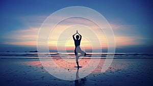Silhouette of young woman practicing yoga on the beach at amazing sunset. Meditation