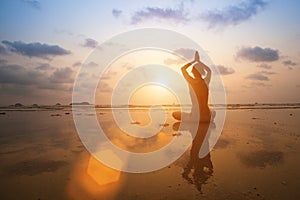 Silhouette young woman practicing yoga on the beach sea at sunset.