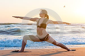 Silhouette of a young woman practicing yoga on the beach at sunrise. Sport, wellness concept