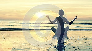 Silhouette young woman practicing yoga on beach at sunset .