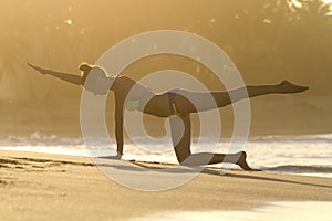 Silhouette young woman practicing yoga on the beach at sunset