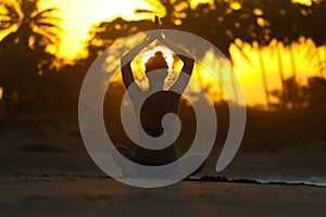 Silhouette of a young woman practicing yoga on the beach at sunset