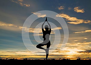 Silhouette young woman practicing yoga on the beach in sunset.