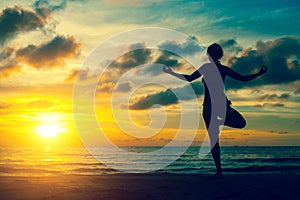 Silhouette young woman practicing yoga on the beach