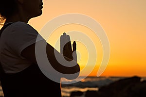 Silhouette young woman practicing yoga on the beach at sunset.