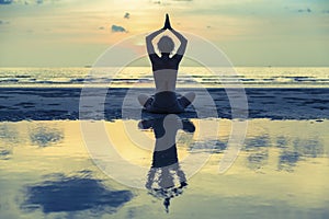 Silhouette young woman practicing yoga on the beach at surrealistic sunset.