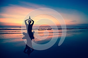 Silhouette young woman practicing yoga on the beach at surrealistic sunset. Relax.