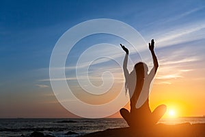 Silhouette of young woman practicing yoga on the sea beach