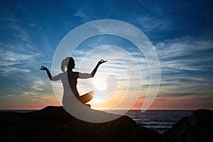 Silhouette young woman practicing yoga on the sea beach