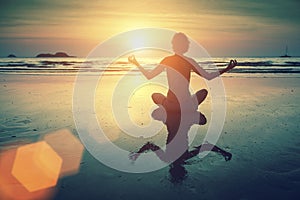 Silhouette young woman practicing yoga on the sea beach at amazing sunset. Relax.