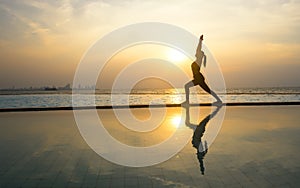 Silhouette young woman practicing yoga on swimming pool and the beach
