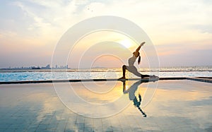 Silhouette young woman practicing yoga on swimming pool