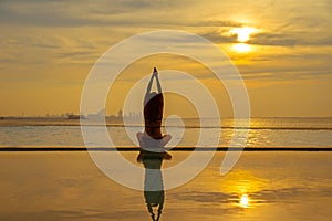 Silhouette young woman practicing yoga on swimming pool and the beach at sunset