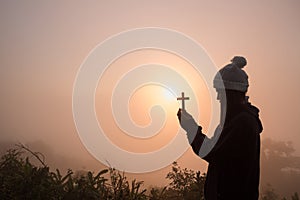 Silhouette of young woman praying with a cross at sunrise, Christian Religion concept background