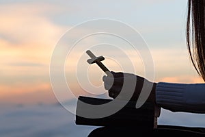 Silhouette of young woman praying with crosses and bibles at sunrise, Christian Religion concept background