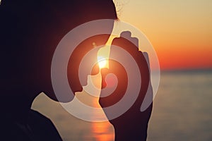 Silhouette of young woman raising hands praying at sunset or sunrise light, practicing yoga on the beach,
