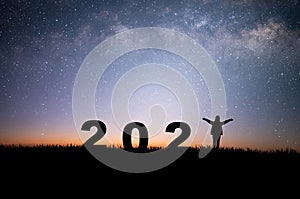 Silhouette of young woman raising hands prepare to welcome the new year 2022 and looking view night sky, star and milky way alone