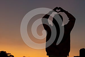 A silhouette of a young woman raising her hands above her head to represent a heart symbol signifying friendship, love and