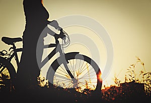 Silhouette of young woman riding bike at sunset