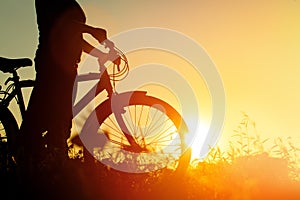 Silhouette of young woman riding bike at sunset