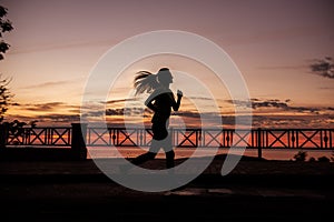 Silhouette of young woman running along the road along the sea early in the morning at dawn of sun