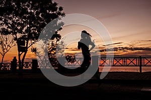 Silhouette of young woman running along the road along the sea early in the morning at dawn of sun