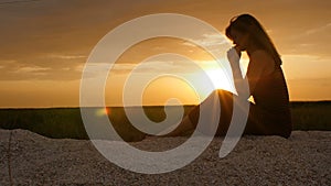 Silhouette of a young woman on the sand at sunset, girl praying to the god on horizon, the concept of vacations, religion, the bea