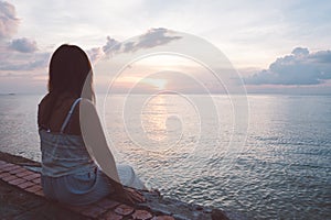 Silhouette of young woman sitting alone on back side outdoor at