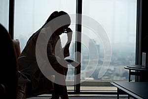 silhouette of a young woman sitting on a sofa spending time alone at home, young upset pensive woman feeling lonely or frustrated