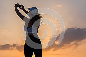 Silhouette young woman in the sport clothes and mobile phone taking picture sunset sky. The concept of healthy lifestyle.