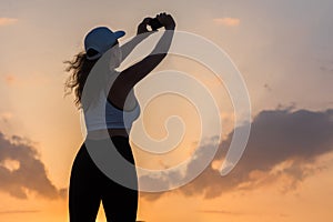 Silhouette young woman in the sport clothes and mobile phone taking picture sunset sky. The concept of healthy lifestyle.