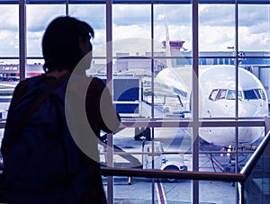 Silhouette a young woman is standing at the airport by the window looking at the pre-flight preparation of the aircraft.