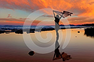 Silhouette of young woman standing on the beach at the sunset
